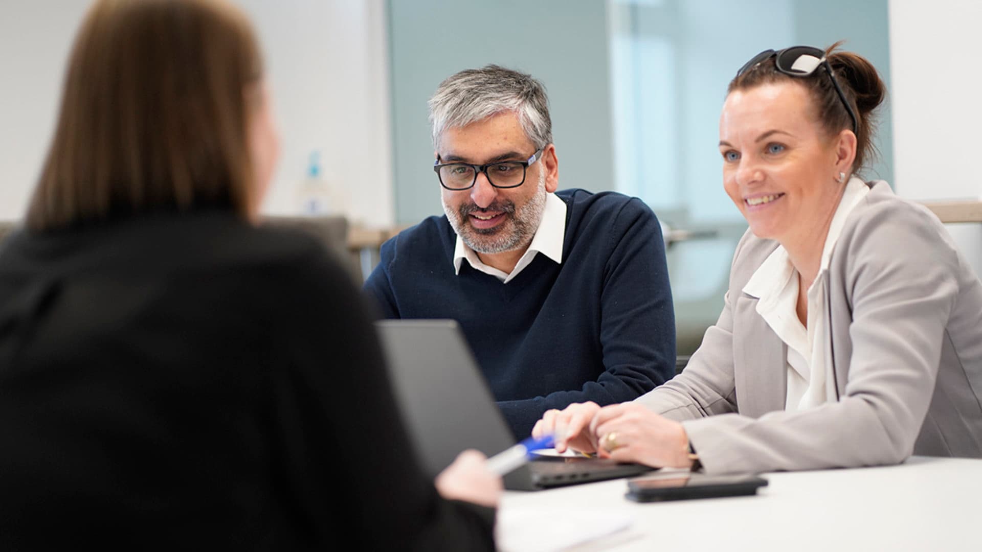 Members of the company meeting around a table with notebooks and laptops