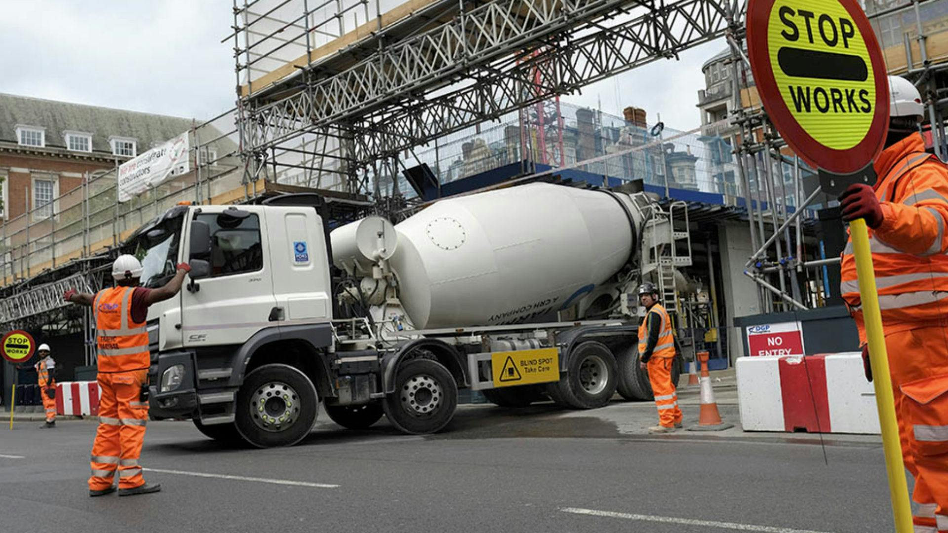 Lorry exiting a building site with workmen guiding them out and stopping traffic