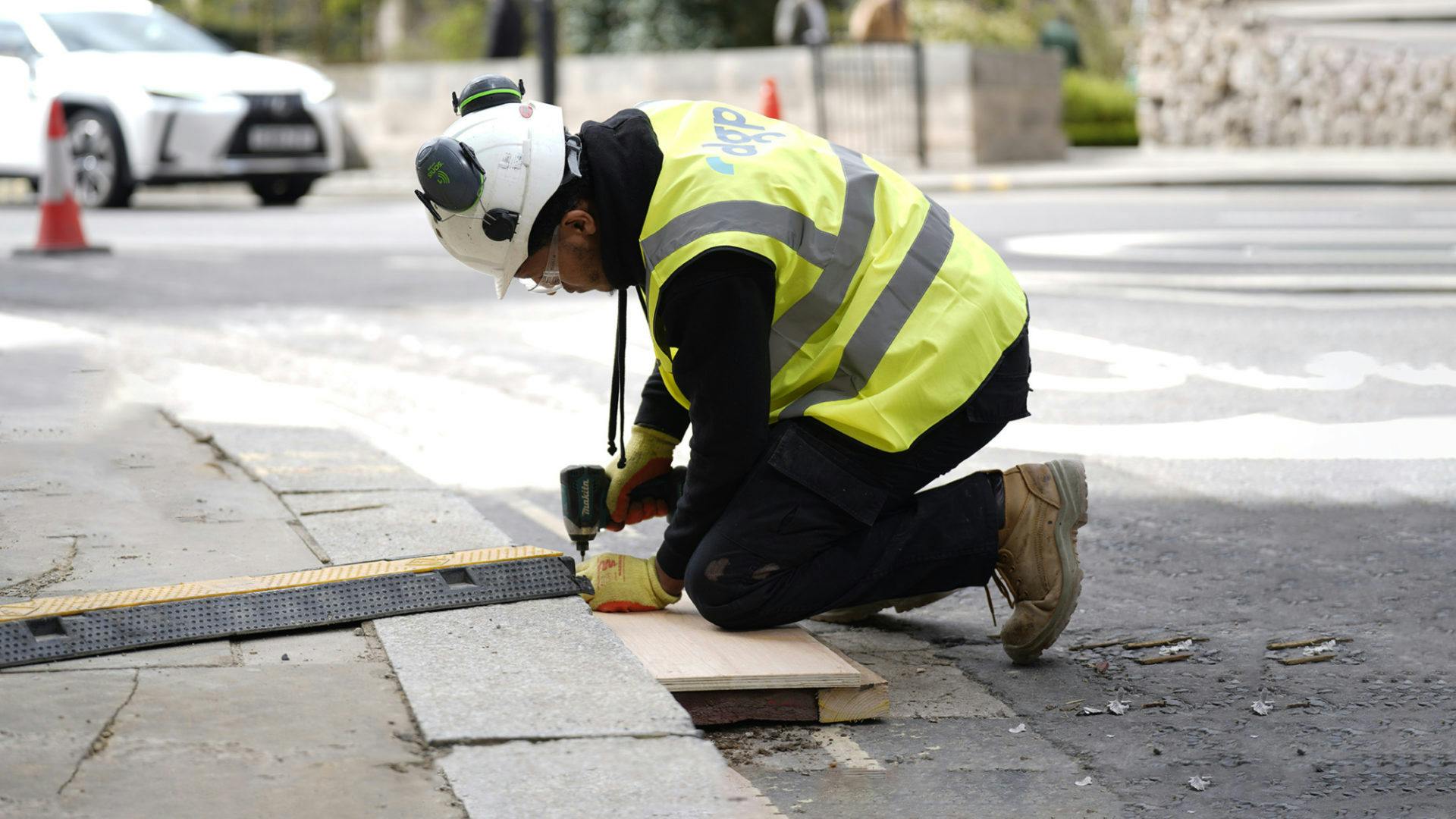 Construction worker in PPE securing a cable ramp to the pavement