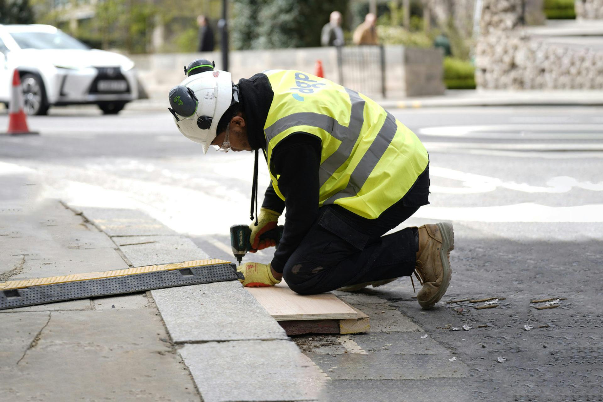 Construction worker in PPE securing a cable ramp to the pavement